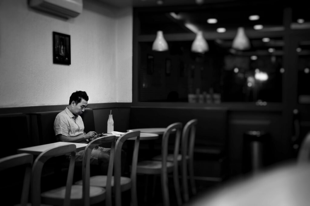 B&W image of a masc-presenting sitting alone in an empty cafe